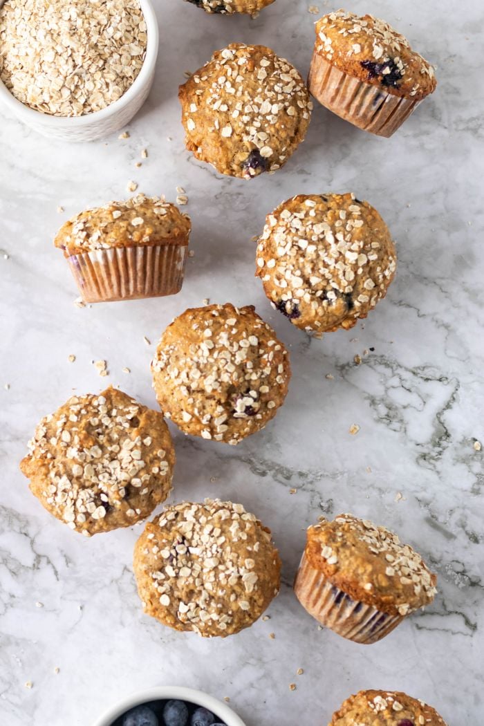 banana blueberry oatmeal muffins are scattered along a marble counter